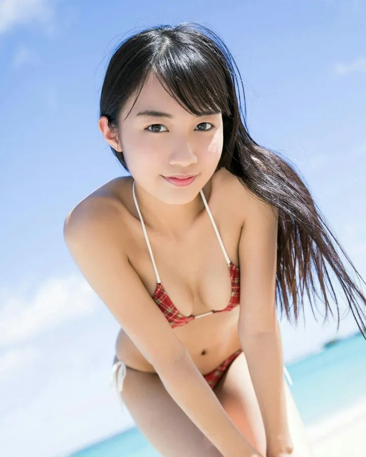 Jeune femme asiatique en maillot de bain rouge à carreaux, assise sur le sable, regardant l'objectif.