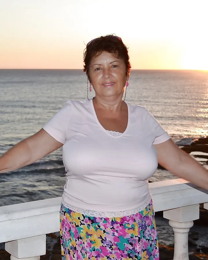 Femme en haut blanc, regardant vers le ciel, debout sur un balcon avec une vue sur un bâtiment à dôme au coucher du soleil.