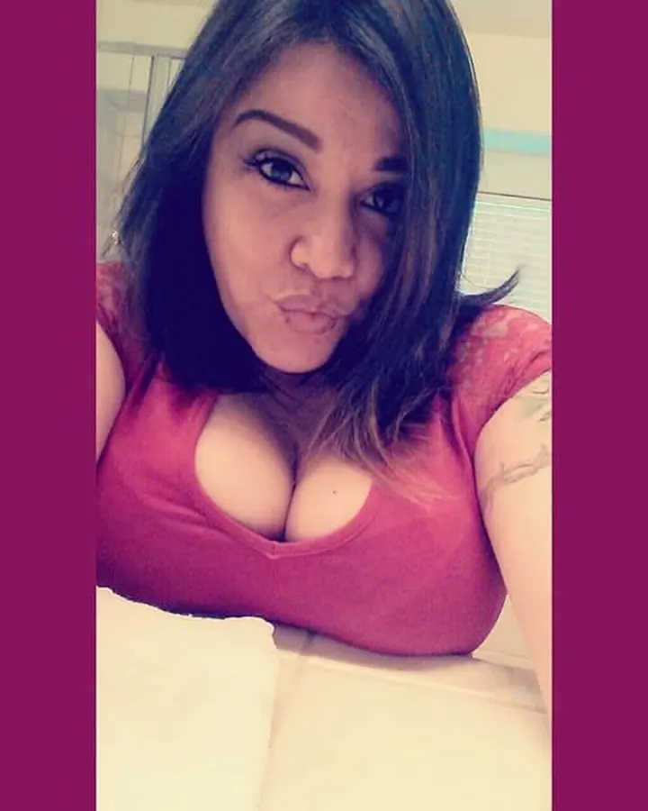 Femme en haut rose, regardant directement l'appareil photo avec une expression suggestive, les seins visibles.