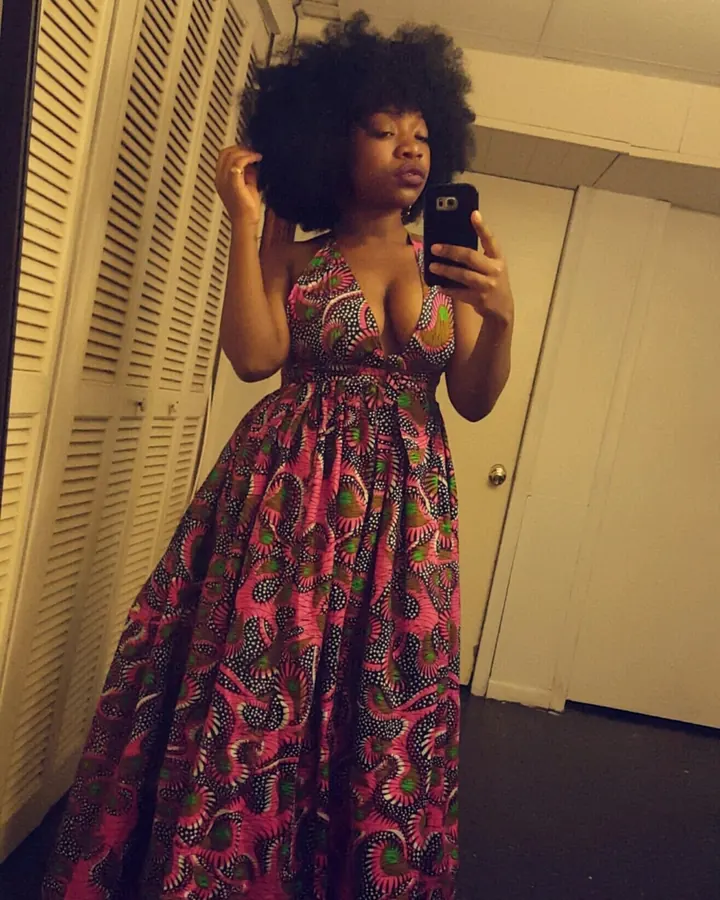 Femme noire aux cheveux afro en robe longue colorée, prenant un selfie devant un miroir.