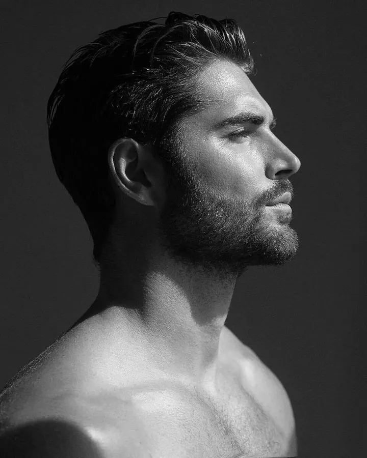 Portrait en noir et blanc d'un homme torse nu, profil, barbe soignée, cheveux coiffés