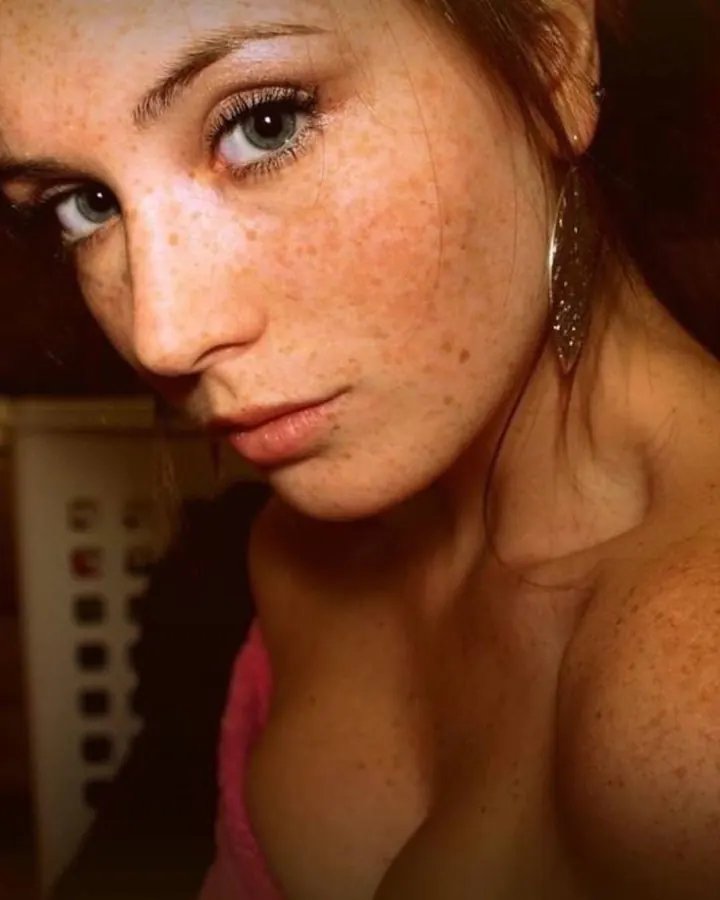 Femme aux yeux verts et cheveux roux, regardant directement l'appareil photo, peau couverte de taches de rousseur.