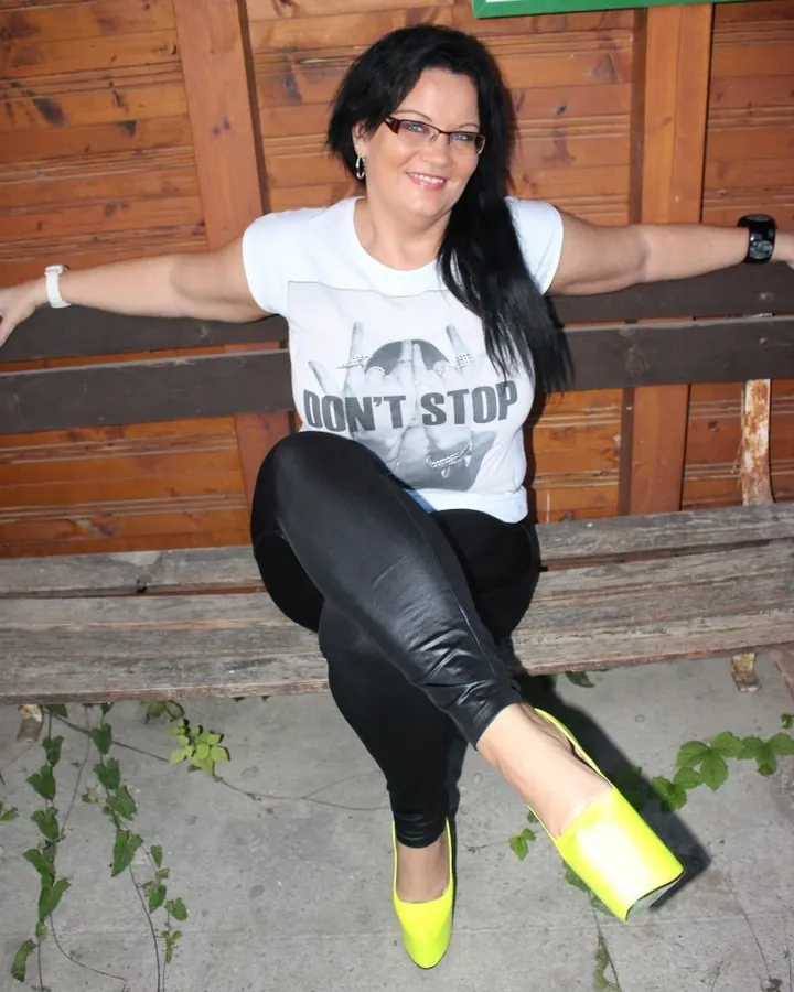 Femme aux cheveux noirs portant un t-shirt blanc avec l'inscription 'DON'T STOP' et des bottes jaunes vives, assise sur un banc en bois.