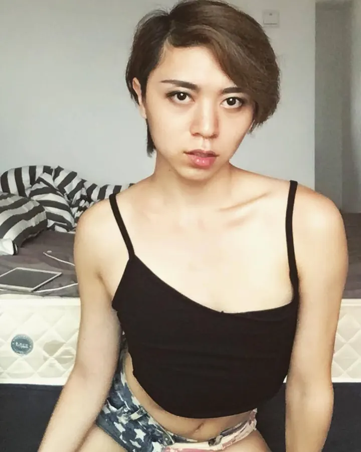 Femme asiatique aux cheveux noirs, portant un haut noir, posant dans une chambre.