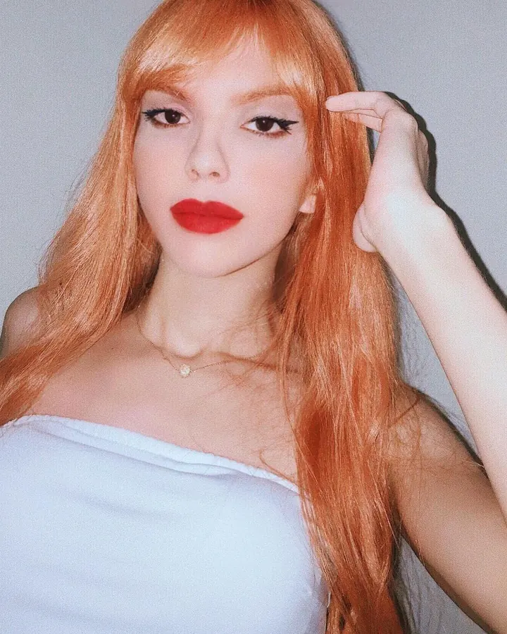 Femme européenne aux cheveux roux longs, vêtue d'un haut léopard, regardant directement l'appareil dans un cadre sombre, expression neutre.