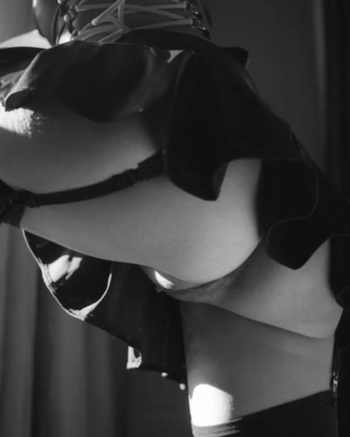 Femme nue de dos, vue de profil, portant un string noir, debout près d'une fenêtre