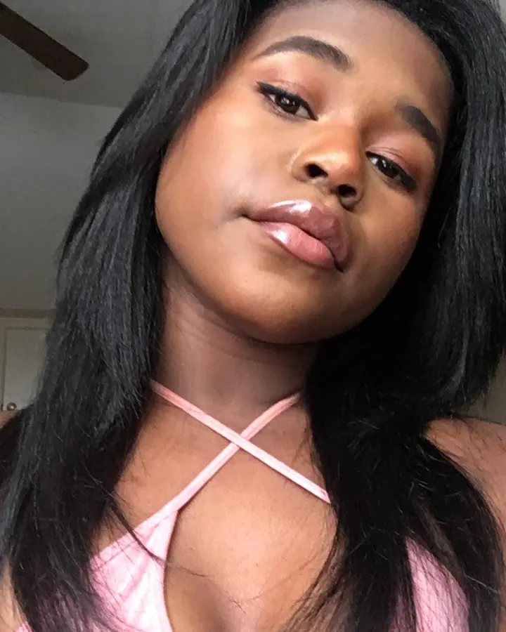 Femme aux cheveux noirs en haut rose croisé, regardant l'appareil photo avec un léger sourire.