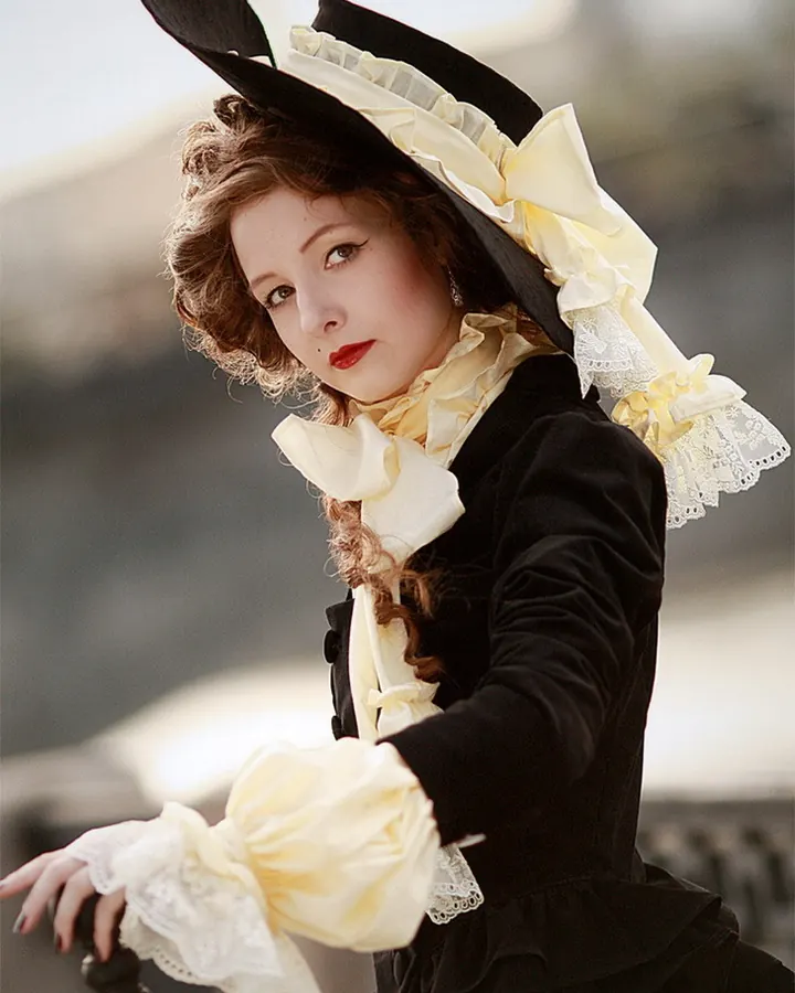 Femme aux cheveux roux en costume victorien noir et jaune, portant un chapeau orné de rubans, appuyée sur une rambarde.