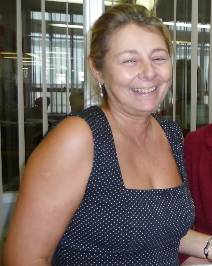 Femme souriante en robe noire à pois, posant devant une vitrine en intérieur.